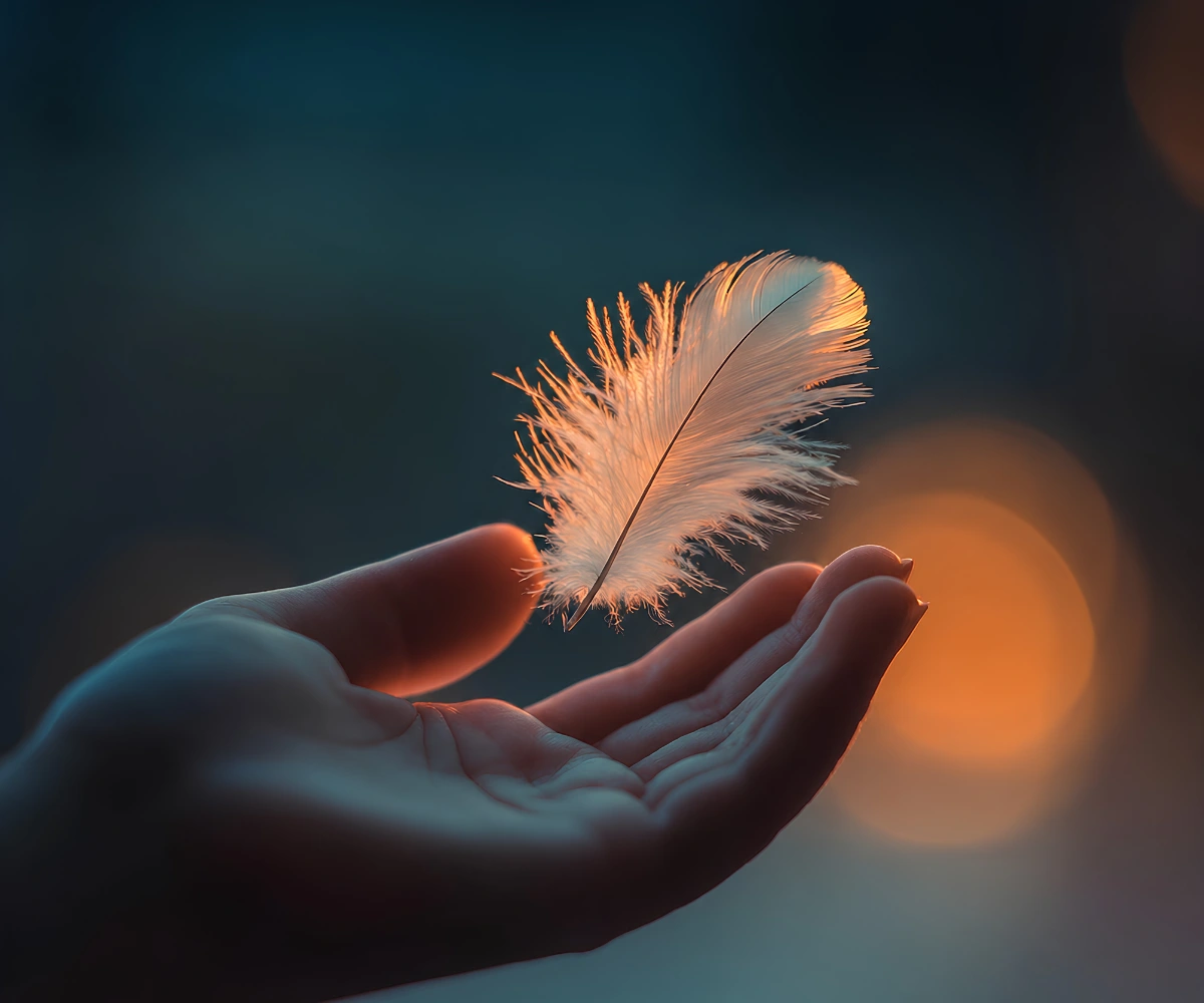 Hand holding a floating and glowing feather symbolizing peace and emotional healing