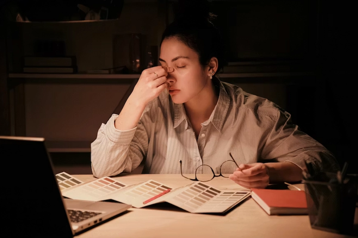 Woman feeling mentally exhausted while working at a desk with papers and a laptop