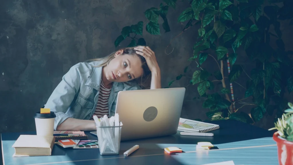 Stressed person sitting at a desk with head resting in hands,very upset because of ADHD next to a laptop, representing the internal struggle of ADHD task paralysis.
