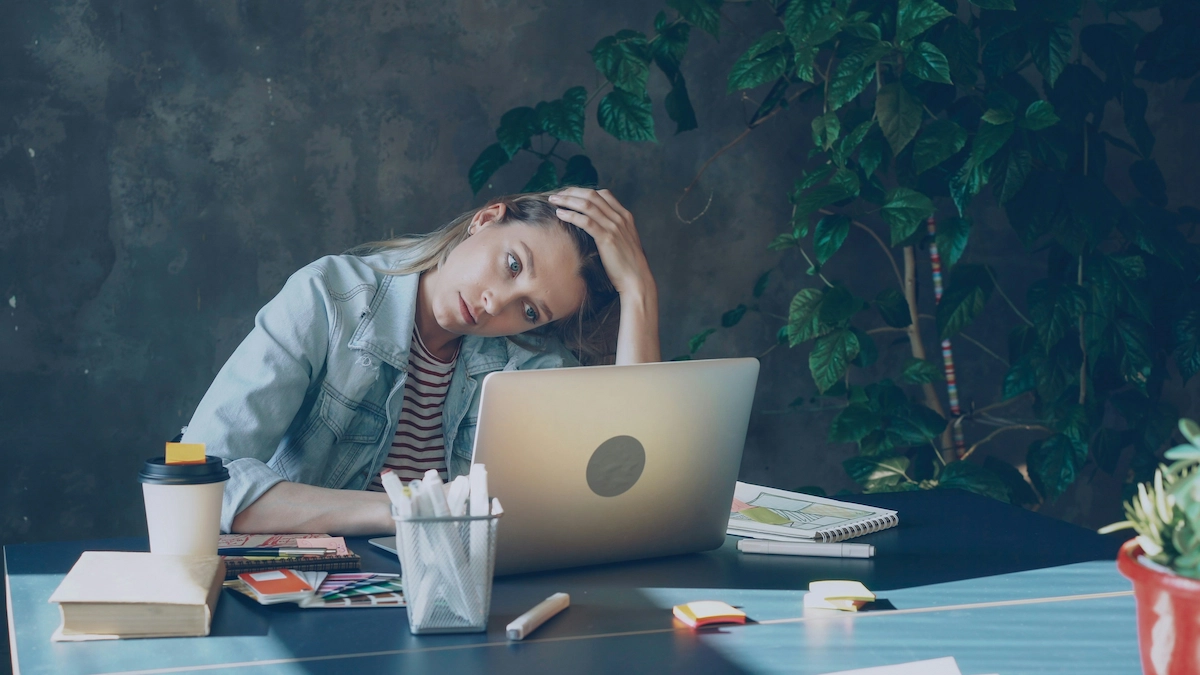 Stressed person sitting at a desk with head resting in hands,very upset because of ADHD next to a laptop, representing the internal struggle of ADHD task paralysis.